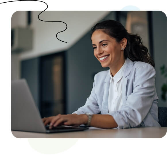 Eine Frau sitzt an einem Schreibtisch und tippt auf einem Laptop vor einem Whiteboard.