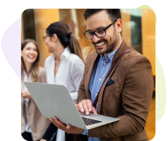 Ein Mann mit Brille und Laptop, der fröhlich lächelnd an seinem Computer arbeitet.