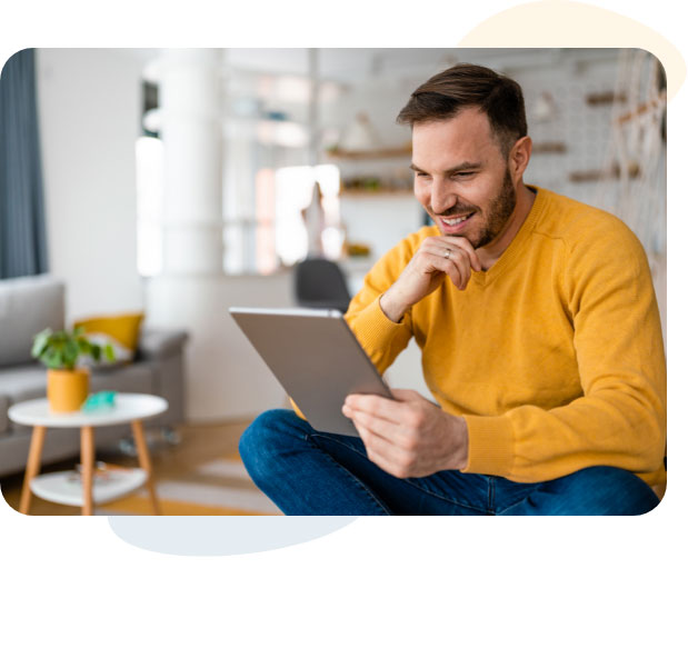 Mann sitzt auf der Couch im Wohnzimmer und benutzt ein Tablet.
