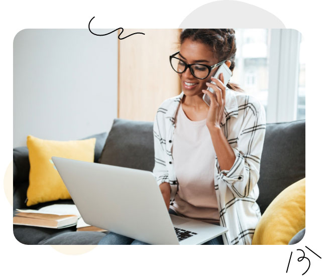Eine Frau mit Brille sitzt auf einer Couch, hält einen Laptop und ein Telefon in den Händen und betreibt effizientes Multitasking.