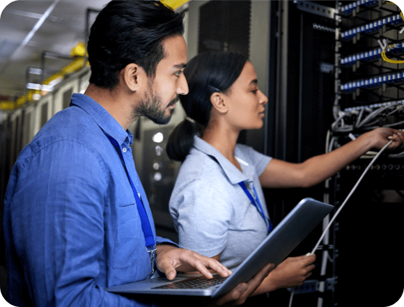 Zwei Techniker, die in einem Rechenzentrum an einem Server zusammenarbeiten, umgeben von Reihen von Geräten und blinkenden Lichtern.